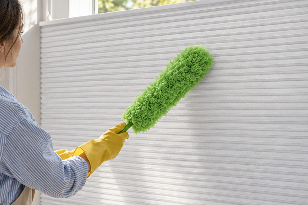 Woman using a green microfiber duster to gently clean white cellular shades.