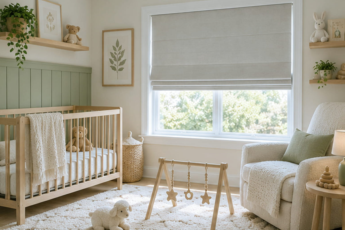 A gray Roman shade hangs beside a wooden crib in a nursery with sage green paneling and a cream armchair.