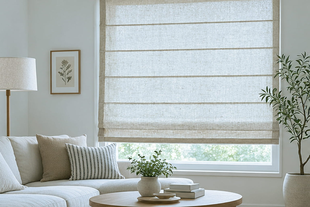 A wide textured Roman shade sits inside a large window frame beside a sofa and round coffee table.