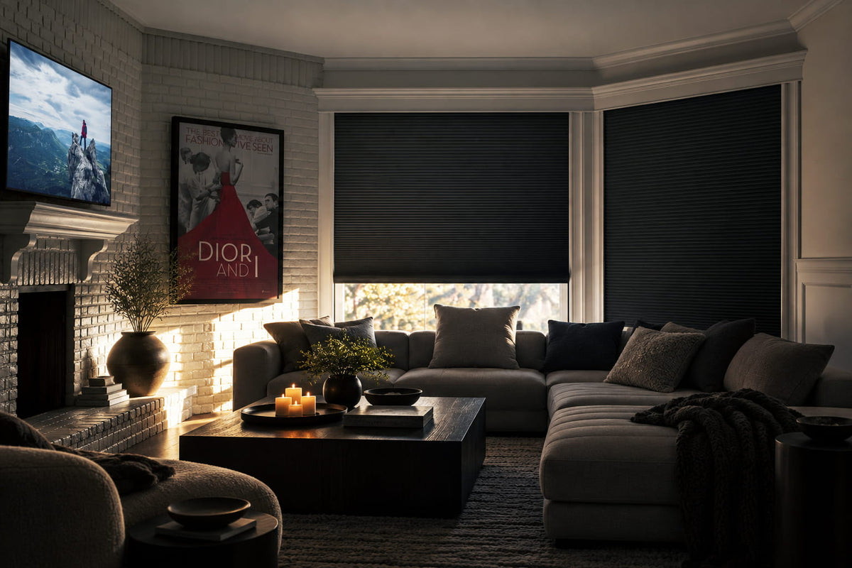 Dark pleated shades in a media room with a wall-mounted television, a dark sectional sofa and a coffee table.
