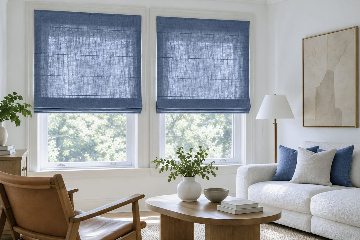 Two blue Roman shades extend beyond the window recesses behind a white sofa and wooden lounge chair.