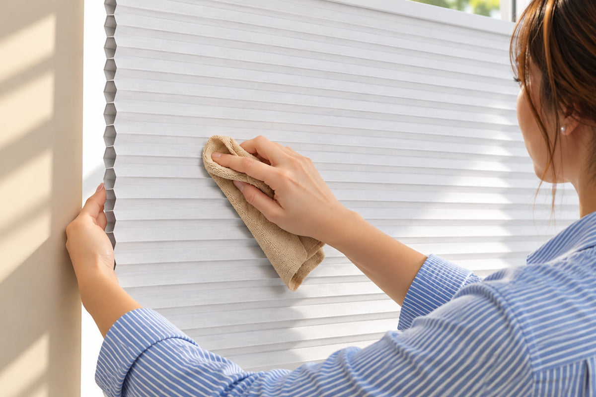 Woman holding a soft cloth against a white cellular shade near its honeycomb edge.
