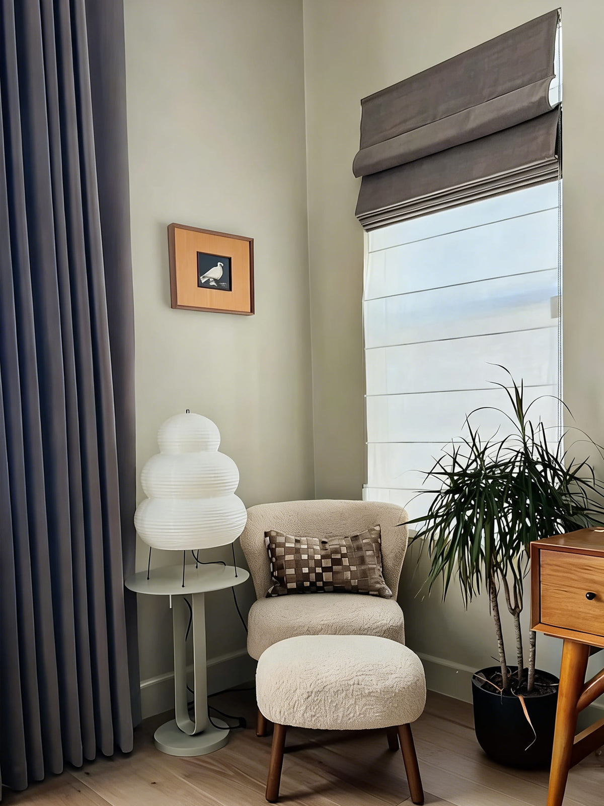 Dark Roman shade beside curtains and a reading chair