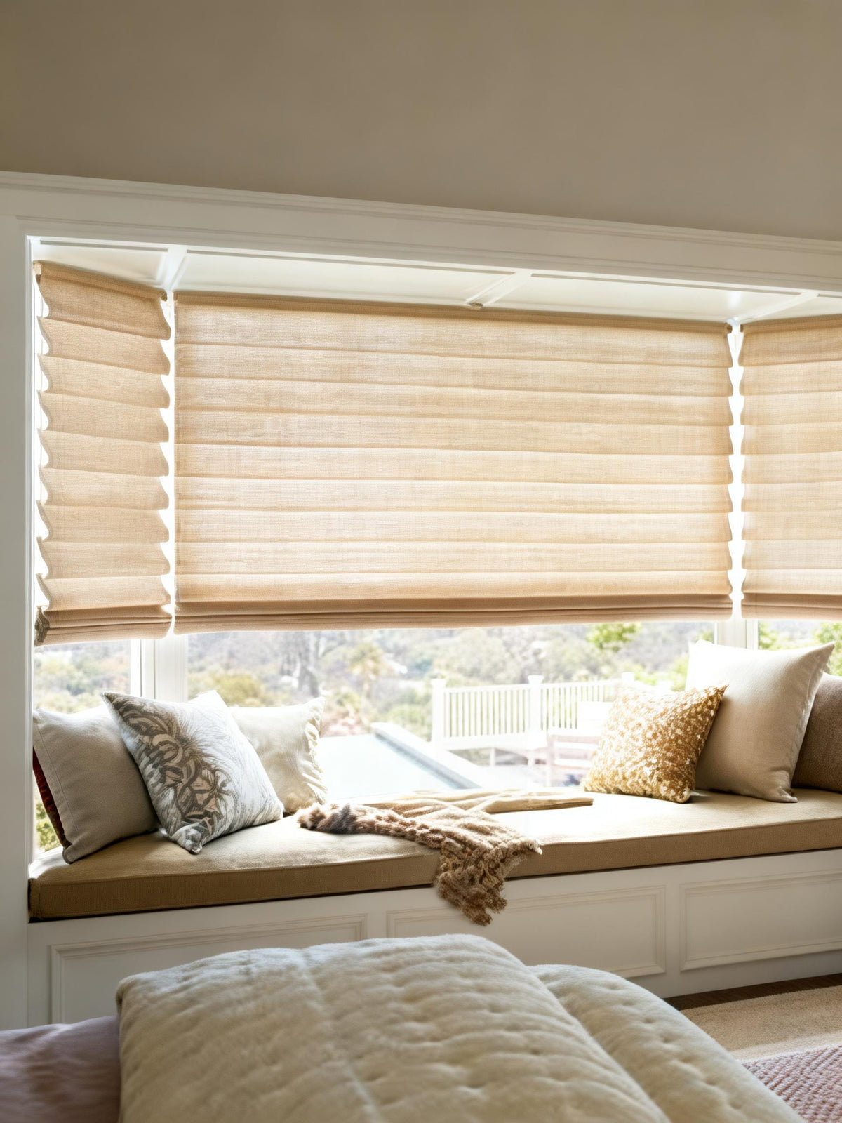 Beige Roman shades above a cushioned window seat