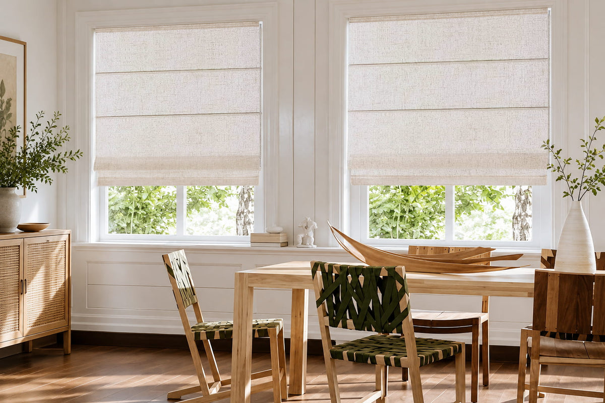 Off-white waterproof polyester Roman shades with a finely woven texture filter soft daylight into a bright dining room with natural wood furniture.