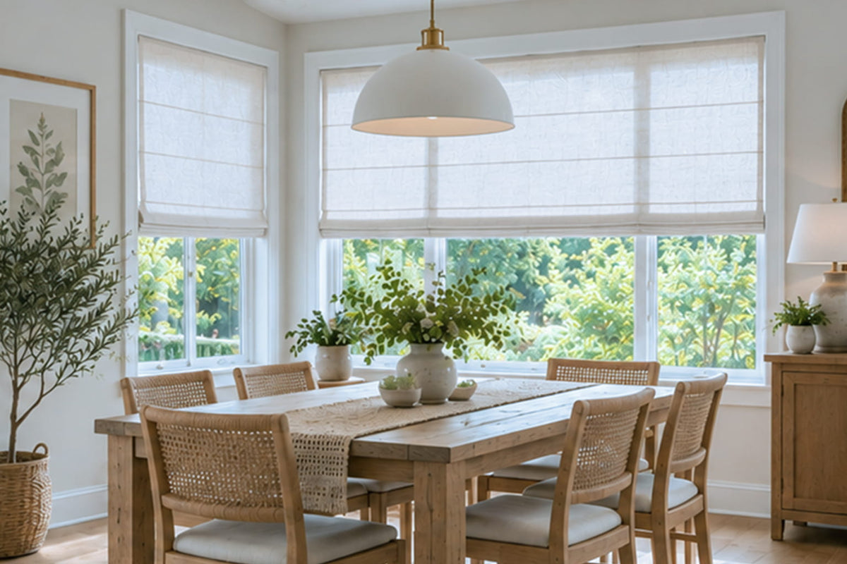 A wide white Roman shade spans the main window beside a wooden dining table and woven chairs.